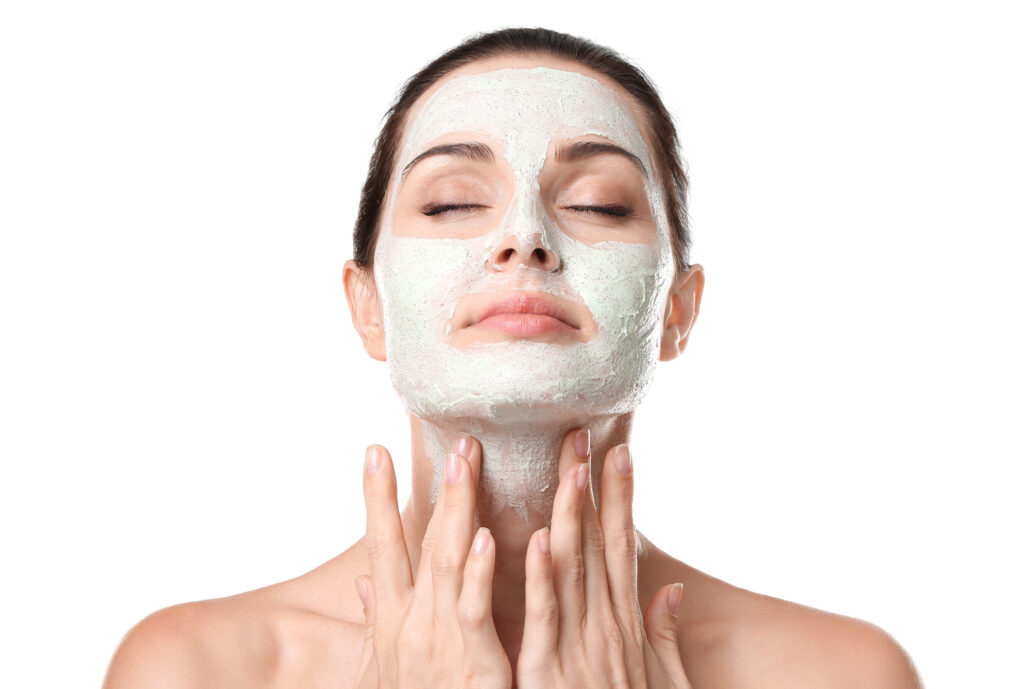 Beautiful young woman applying scrub mask on face, closeup